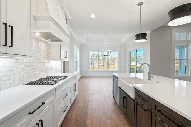 kitchen with white cabinets, custom range hood, hanging light fixtures, a tray ceiling, and a sink