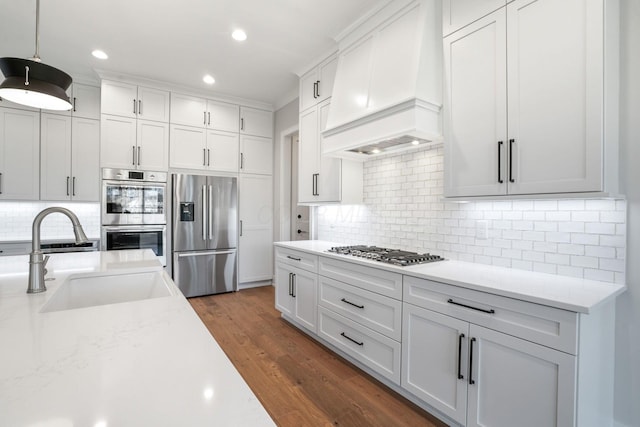 kitchen with stainless steel appliances, a sink, white cabinetry, custom range hood, and pendant lighting