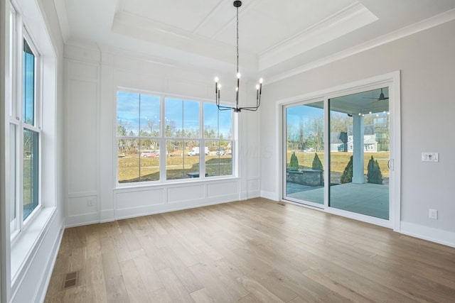 unfurnished dining area with ornamental molding, a tray ceiling, a decorative wall, and light wood-style flooring