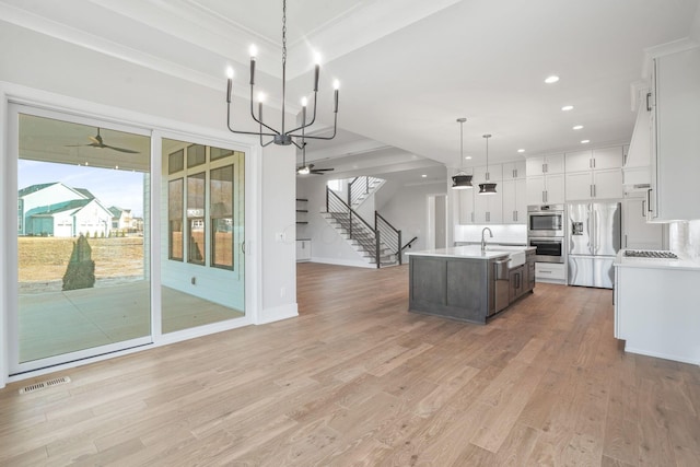 kitchen with visible vents, appliances with stainless steel finishes, a kitchen island with sink, light countertops, and white cabinetry