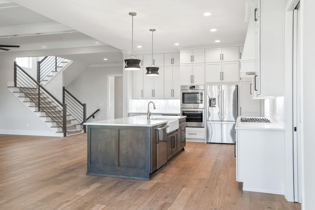 kitchen featuring pendant lighting, light countertops, appliances with stainless steel finishes, a kitchen island with sink, and white cabinetry