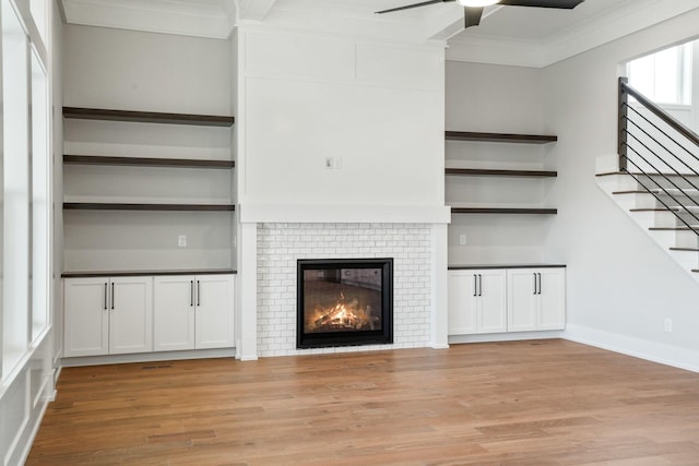 unfurnished living room featuring ceiling fan, light wood-type flooring, a brick fireplace, and crown molding