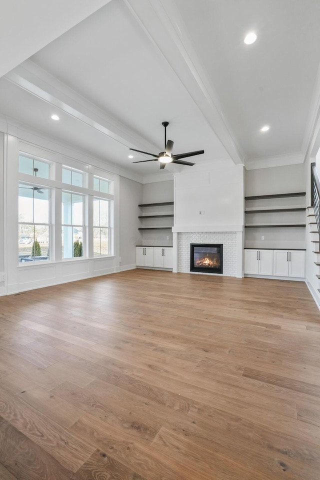 unfurnished living room with ceiling fan, light wood-style flooring, a fireplace, ornamental molding, and beamed ceiling