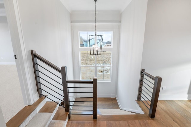 stairs with baseboards, wood finished floors, a wealth of natural light, and a notable chandelier