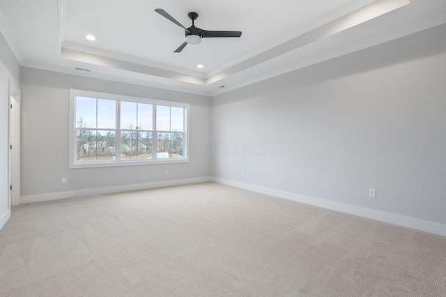 empty room featuring light carpet, baseboards, and a raised ceiling