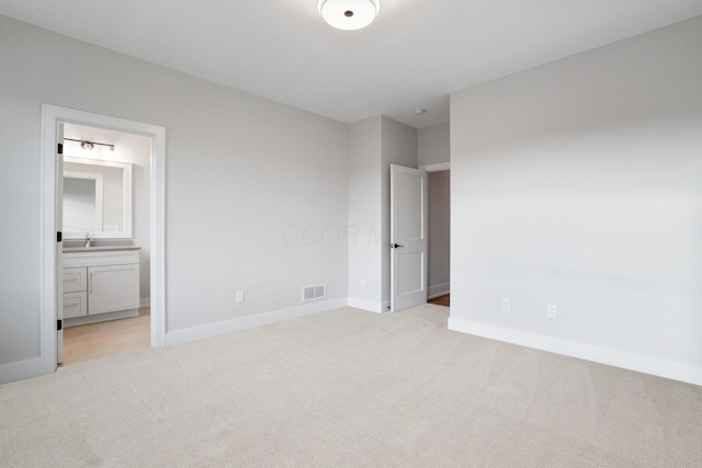 unfurnished bedroom featuring light colored carpet, visible vents, a sink, ensuite bath, and baseboards