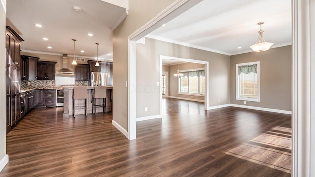 interior space with backsplash, a breakfast bar, wall chimney range hood, decorative light fixtures, and a center island