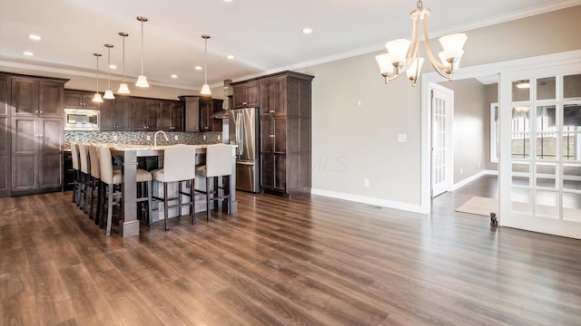 kitchen with pendant lighting, a center island with sink, decorative backsplash, stainless steel appliances, and a chandelier