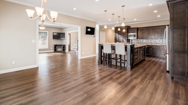 kitchen featuring appliances with stainless steel finishes, backsplash, a kitchen breakfast bar, a kitchen island with sink, and decorative light fixtures