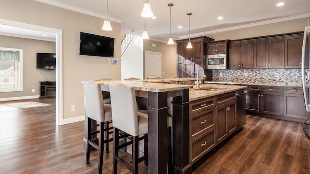 kitchen featuring stainless steel microwave, a kitchen breakfast bar, sink, an island with sink, and decorative light fixtures