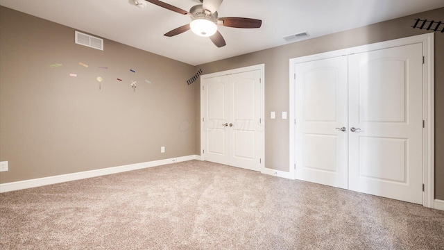 unfurnished bedroom with carpet floors, two closets, and ceiling fan