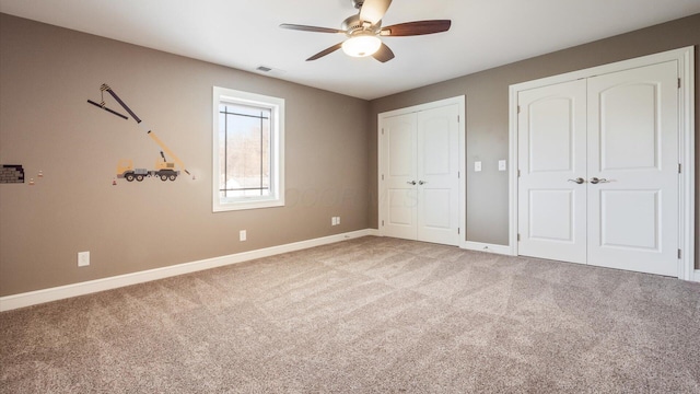 unfurnished bedroom with carpet flooring, ceiling fan, and two closets