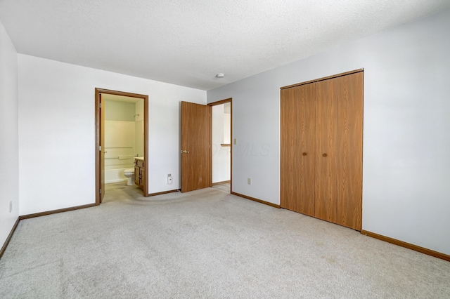 unfurnished bedroom with a textured ceiling, a closet, ensuite bathroom, and light colored carpet