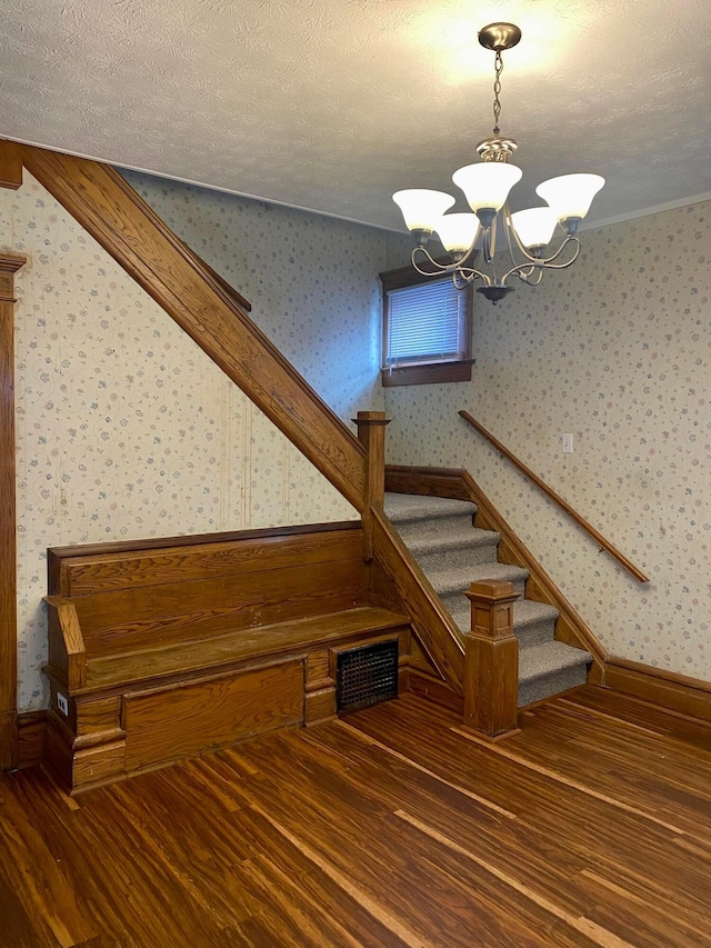 stairs with a textured ceiling, crown molding, hardwood / wood-style flooring, and a notable chandelier