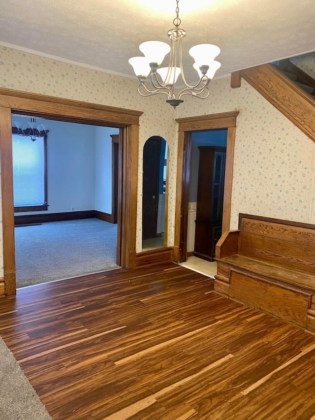 unfurnished room featuring a textured ceiling, dark wood-type flooring, crown molding, and a chandelier