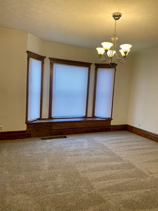 carpeted spare room with a textured ceiling and a chandelier