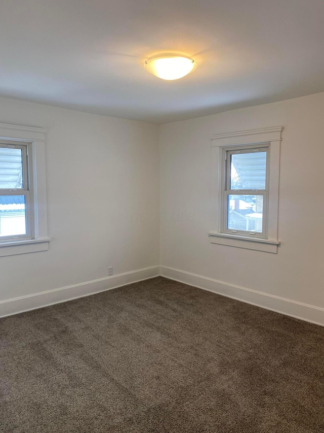 spare room with dark colored carpet and a healthy amount of sunlight