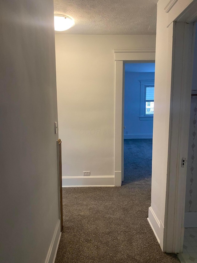 hall featuring a textured ceiling and dark colored carpet