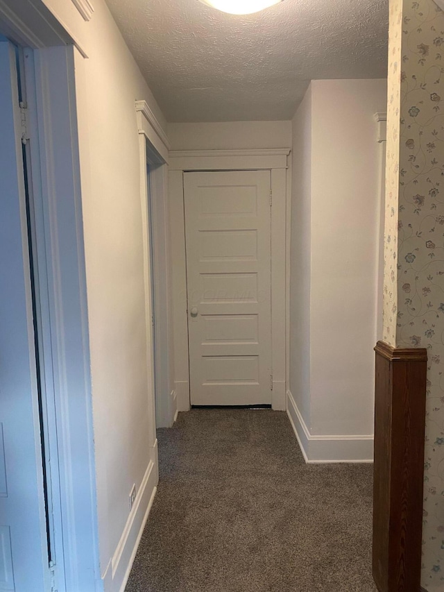 hall featuring a textured ceiling and dark carpet