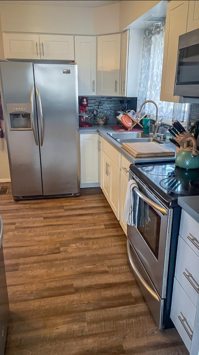 kitchen featuring sink, dark wood-type flooring, tasteful backsplash, white cabinets, and appliances with stainless steel finishes