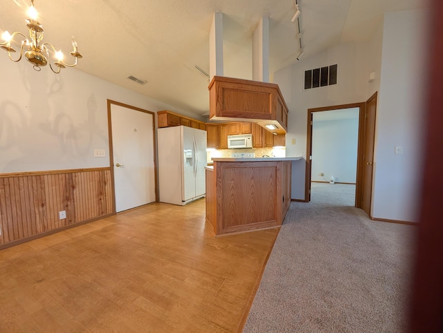 kitchen featuring pendant lighting, lofted ceiling, white appliances, an inviting chandelier, and kitchen peninsula