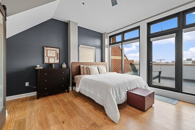 bedroom featuring ceiling fan, a barn door, light hardwood / wood-style floors, lofted ceiling, and access to outside