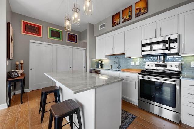 kitchen featuring white cabinets, appliances with stainless steel finishes, a kitchen bar, and a kitchen island