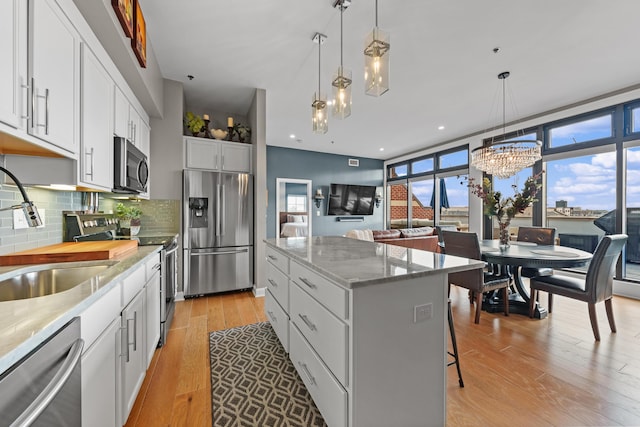 kitchen with pendant lighting, a center island, a wealth of natural light, white cabinetry, and stainless steel appliances