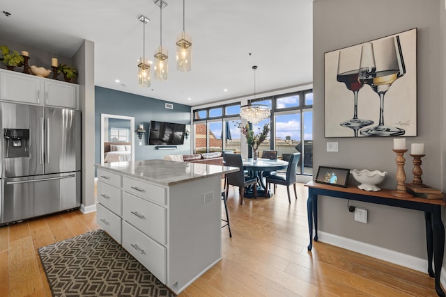 kitchen featuring light stone countertops, stainless steel fridge, white cabinets, and a healthy amount of sunlight