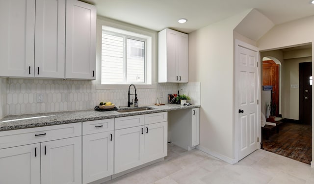 kitchen featuring white cabinets, backsplash, light stone countertops, and sink