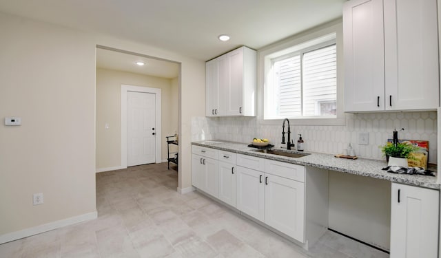 kitchen with tasteful backsplash, white cabinetry, sink, and light stone counters