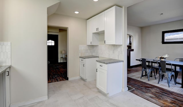 kitchen featuring decorative backsplash, light tile patterned floors, white cabinetry, and light stone countertops