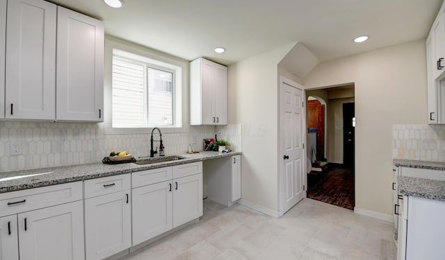 kitchen with decorative backsplash, light stone counters, white cabinetry, and sink