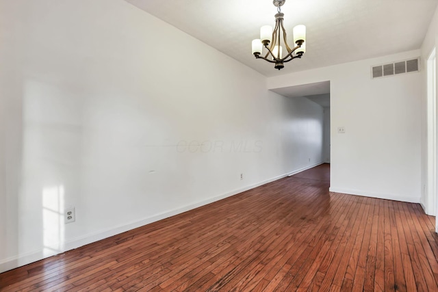 spare room featuring dark hardwood / wood-style floors and a chandelier