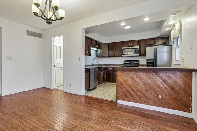 kitchen featuring dark brown cabinetry, stainless steel appliances, an inviting chandelier, light hardwood / wood-style floors, and hanging light fixtures