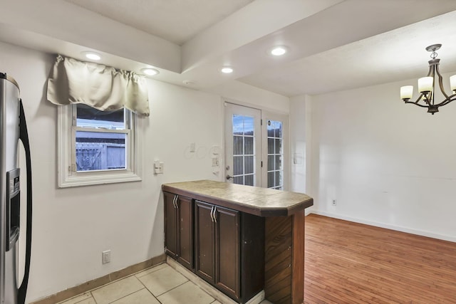 kitchen with stainless steel refrigerator with ice dispenser, decorative light fixtures, dark brown cabinetry, a notable chandelier, and kitchen peninsula
