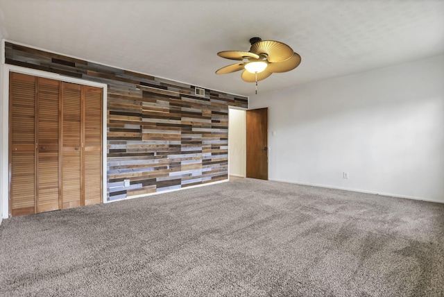 empty room with carpet flooring, wood walls, and ceiling fan
