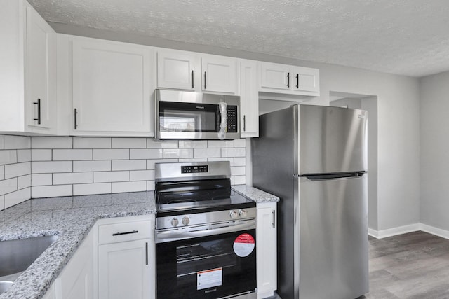 kitchen featuring stainless steel appliances, light stone counters, light hardwood / wood-style flooring, a textured ceiling, and white cabinets