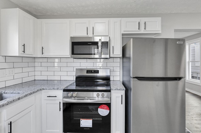 kitchen featuring light stone countertops, tasteful backsplash, a textured ceiling, white cabinets, and appliances with stainless steel finishes