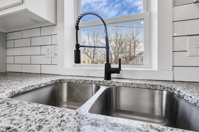 details featuring backsplash, light stone counters, and sink