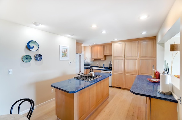 kitchen featuring white appliances, sink, light brown cabinets, a center island, and light hardwood / wood-style floors