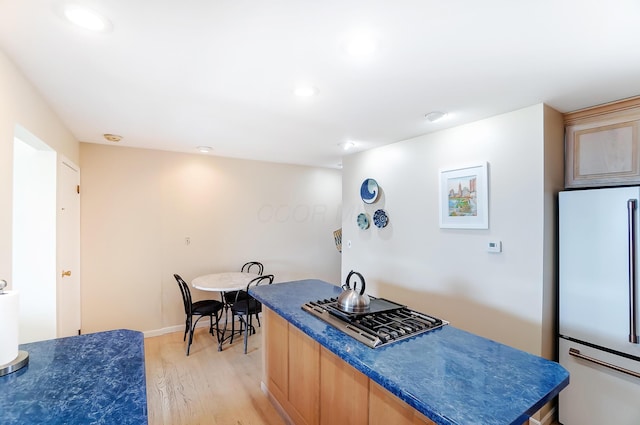 kitchen featuring light brown cabinets, a center island, white fridge, and light hardwood / wood-style floors