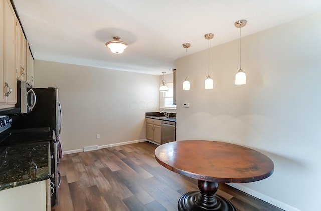 kitchen with sink, dark wood-type flooring, dark stone counters, pendant lighting, and appliances with stainless steel finishes