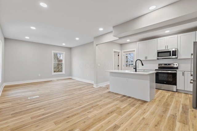 kitchen featuring backsplash, white cabinets, sink, an island with sink, and stainless steel appliances