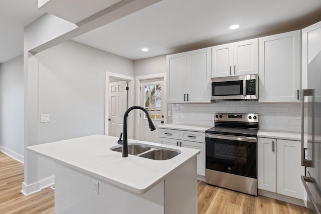 kitchen featuring a kitchen island with sink, sink, decorative backsplash, white cabinetry, and stainless steel appliances