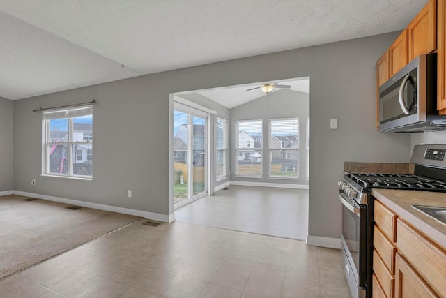 kitchen featuring vaulted ceiling, ceiling fan, a textured ceiling, and appliances with stainless steel finishes