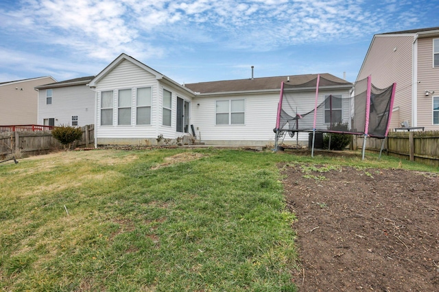 back of house featuring a trampoline and a yard