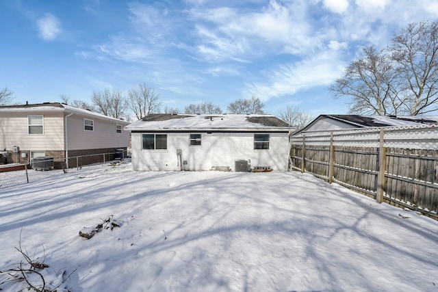 snow covered property with stucco siding, fence, and central air condition unit