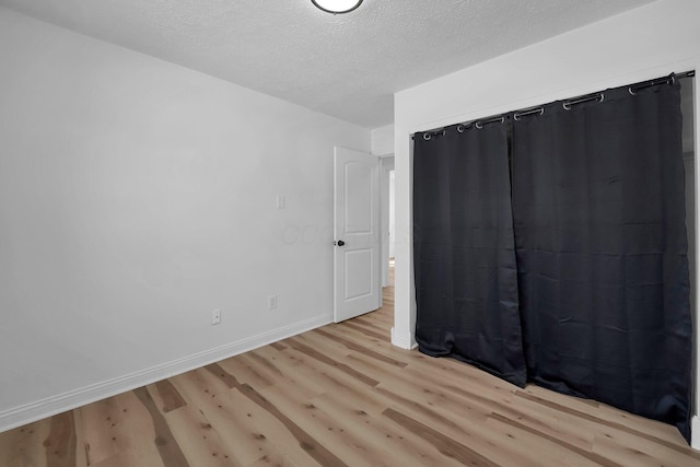 unfurnished bedroom with baseboards, a textured ceiling, and light wood finished floors