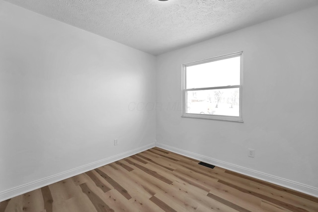 empty room featuring a textured ceiling, light wood finished floors, visible vents, and baseboards